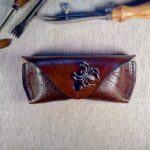 Skórzane etui na okulary na którym wytłoczona jest pajęczyna i siedzi na niej metalowy pająk.