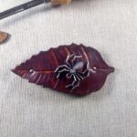 Skórzana spinka do włosów w kształcie liścia, na którym odpoczywa metalowy pająk.