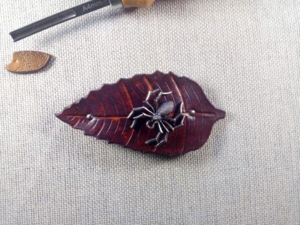 Skórzana spinka do włosów w kształcie liścia, na którym odpoczywa metalowy pająk.
