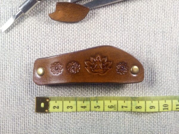 Widok od przodu na skórzaną spinkę do włosów z joginem i miarą krawiecką.