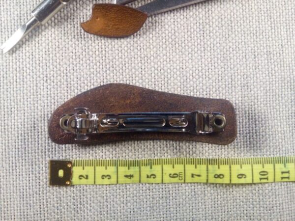 Tył skórzanej spinki do włosów z joginem. Obok rozwinięta miara krawiecka.