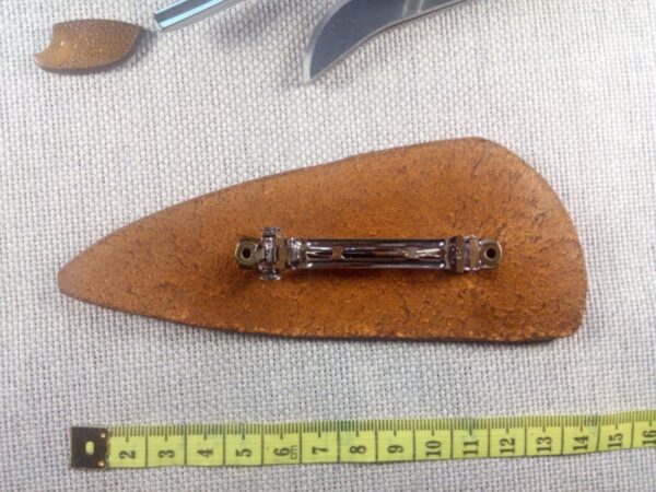 Tył skórzanej spink6i do włosów z wilkiem. Obok jest rozwinięta miara krawiecka dla porównania wielkości spinki.