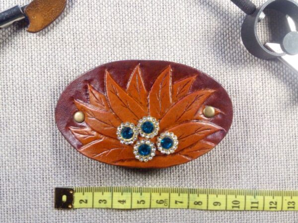 Skórzana spinka do włosów z kwiatem i kryształkami. Widok od przodu z miara krawiecką.